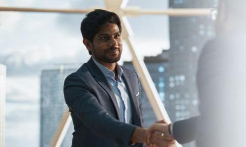 Young MBA business analytics graduate shaking hands with coworker 